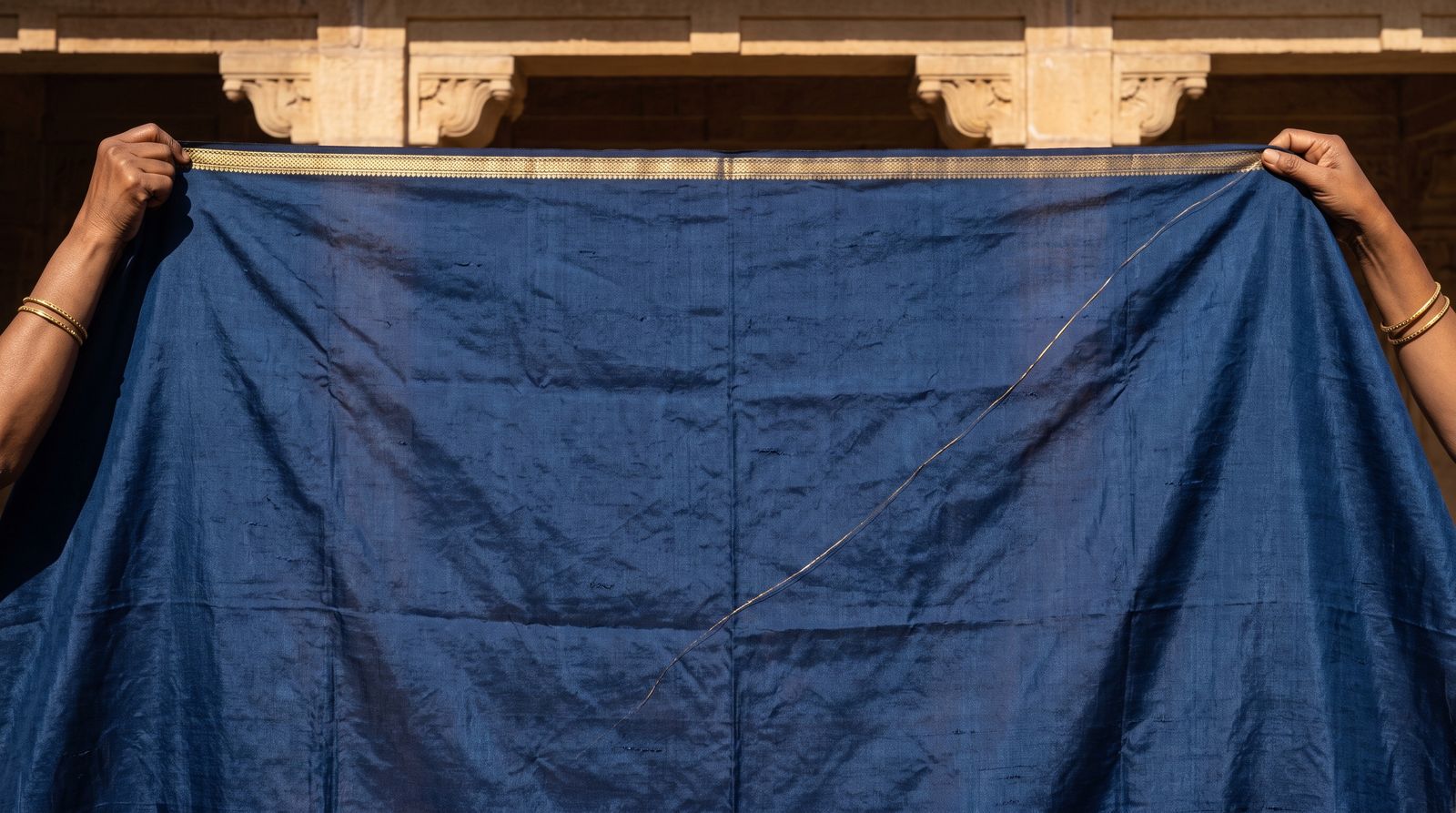 An indigo silk curtain held up in front of a sunlit stone stage