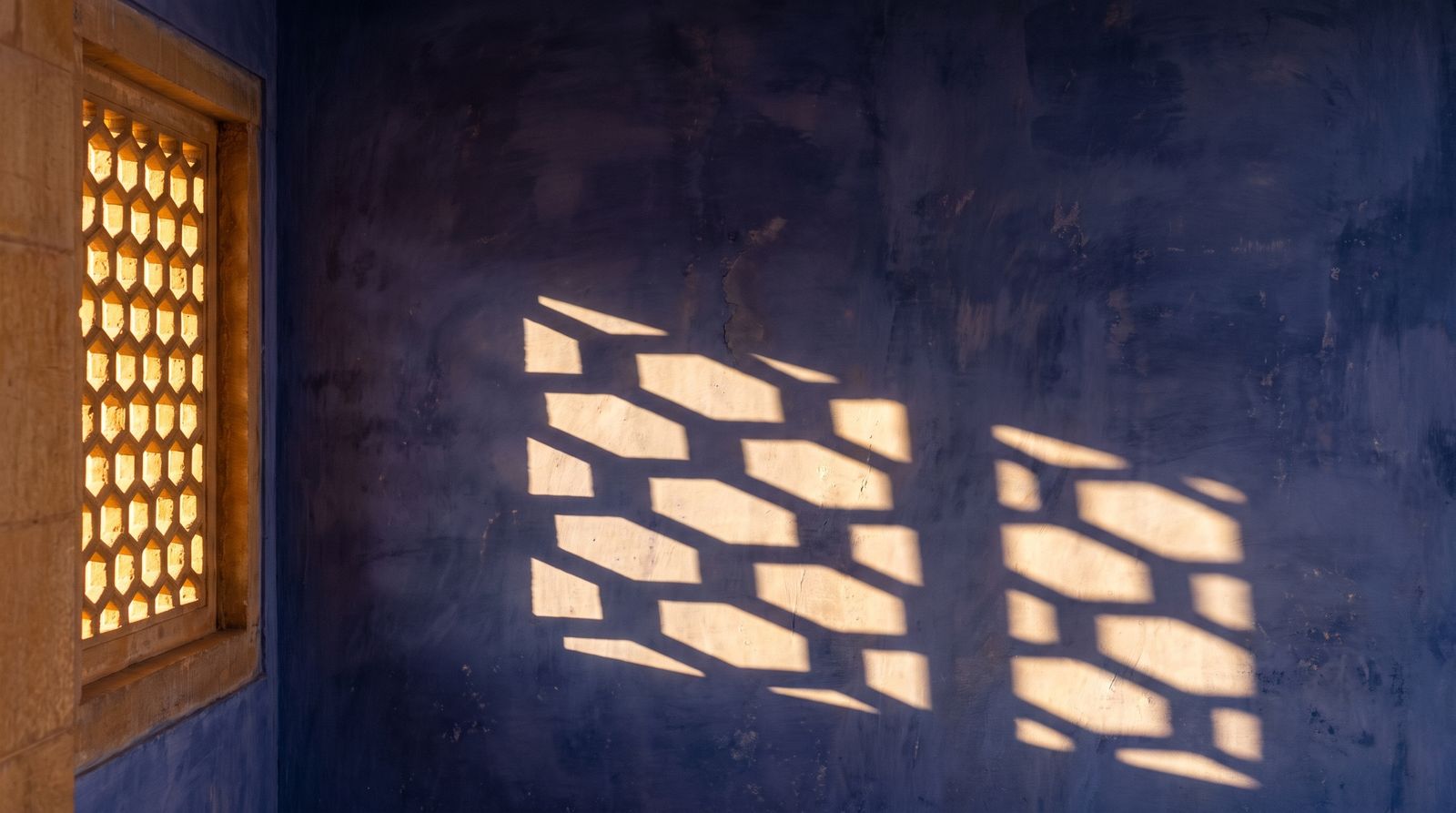 Sunlight through a stone jaali onto an indigo wall
